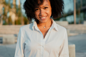 Wall Mural - A close-up portrait of an Afro-looking woman looks into the camera and smiles. The clothing is a classic white shirt.