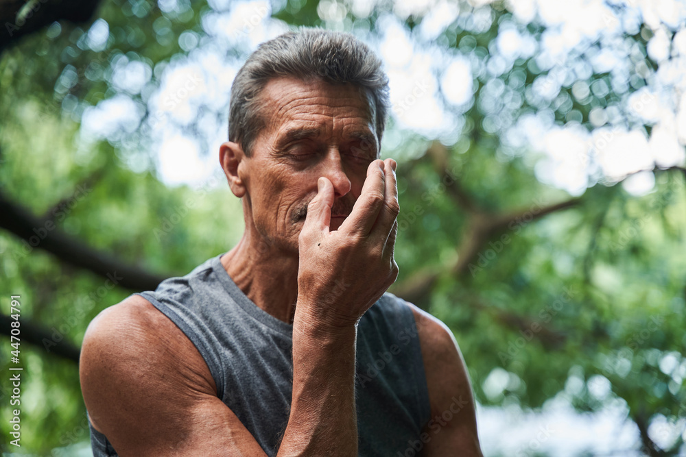 Man keeping his eyes closed and doing breathing exercise while closes nostril with finger - obrazy, fototapety, plakaty 