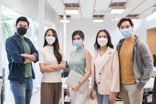 Portrait of Asian creative business team wears face mask. Hipster Creative Startup Young business people in modern office.