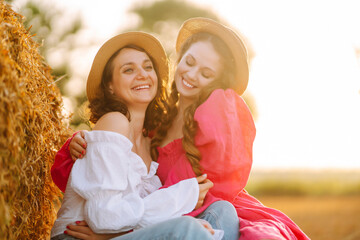 Two young woman in fashionable and stylish clothes posing near hay bales in the countryside. Fashion concept. Nature, vacation, relax and lifestyle.