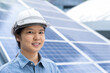 © Bond_JP - Close-up portrait with copy space of a confident Asian woman wearing white safety hard hat and blue shirt, smiling, standing outdoor near solar panels. Female engineer and sustainable energy concept.