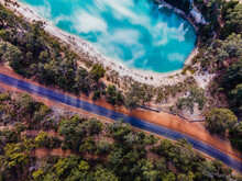 Top View Shot Of Blue Lake With A Sky Reflection, With Green Trees And A Road