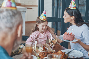 Wall Mural - Happy family celebrating birthday of little girl while sitting at the dining table at home