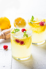 Homemade lemonade with mint and raspberries in glasses, gray tiles background.