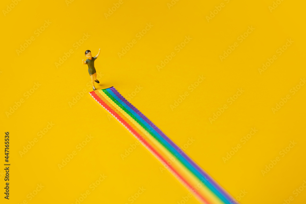 little boy figure stand on rainbow LGBT strip on yellow background - obrazy, fototapety, plakaty 