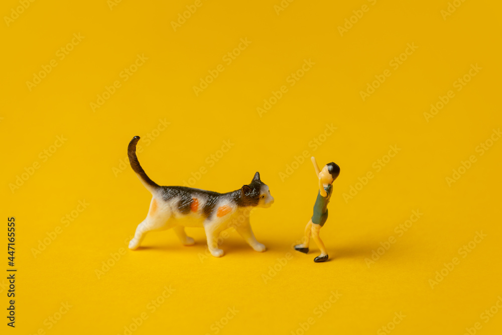 minature figure of boy and cat on yellow background - obrazy, fototapety, plakaty 