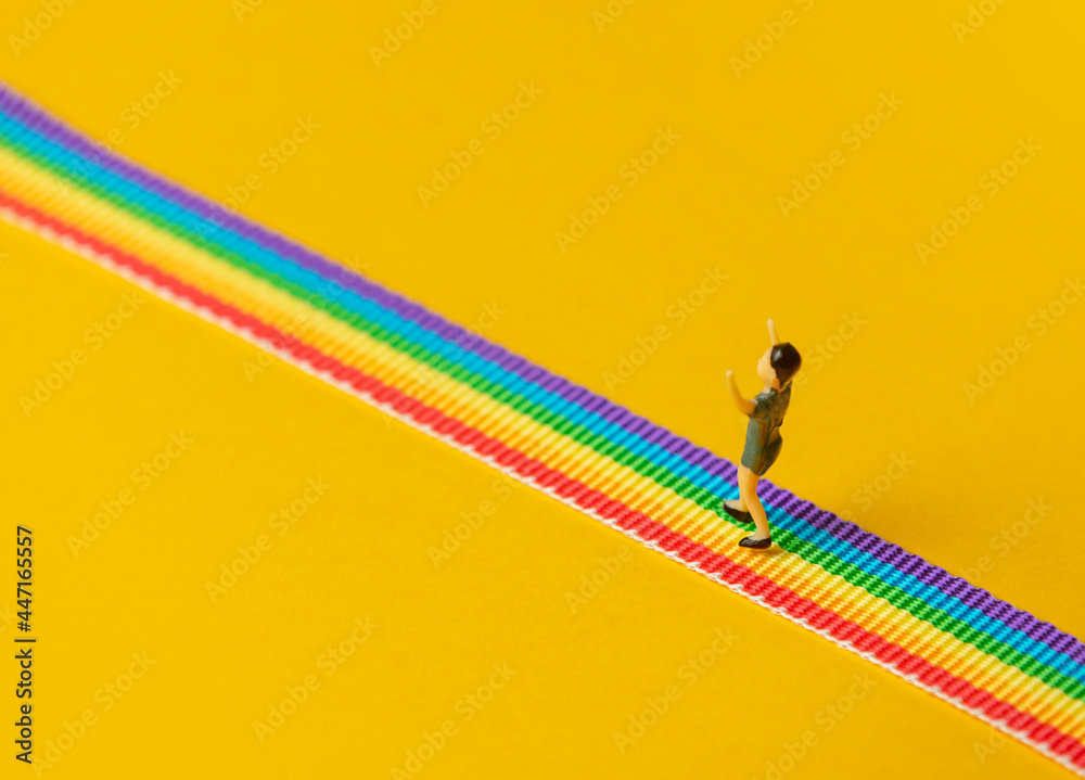 little boy figure stand on rainbow LGBT strip on yellow background - obrazy, fototapety, plakaty 