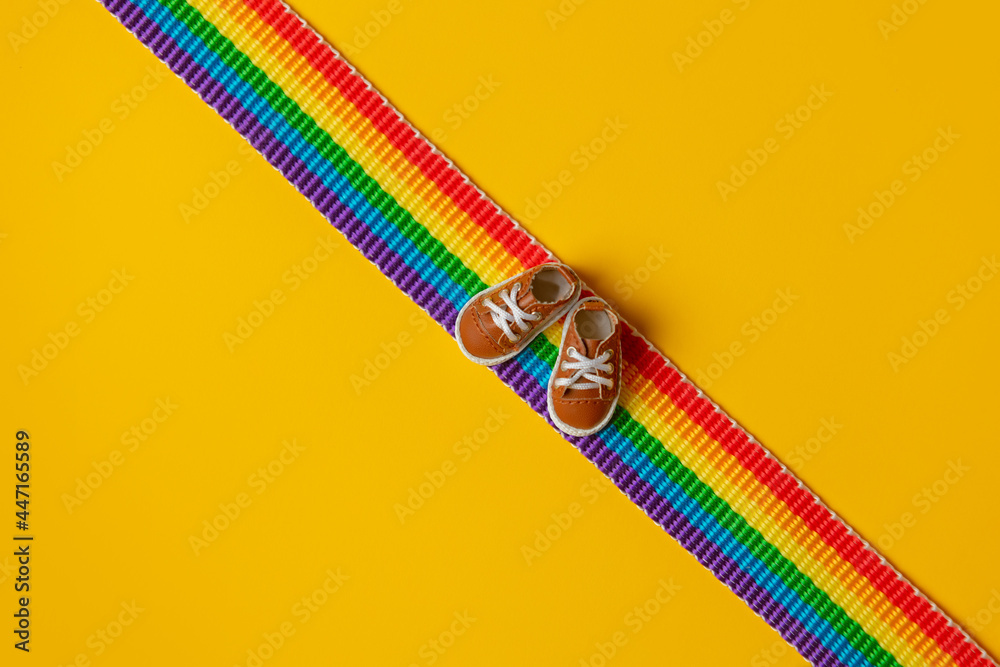Little shoes on LGBT rainbow strip on yellow background - obrazy, fototapety, plakaty 