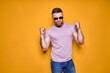 © zamuruev - Image of excited bearded man in sunglasses making winner gesture isolated yellow background
