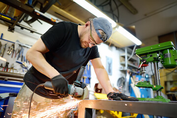 Canvas Print - Metalwork craftsman cutting metal with grinder tools. Worker man in protection gloves and glasses working in the workshop. Small local business.