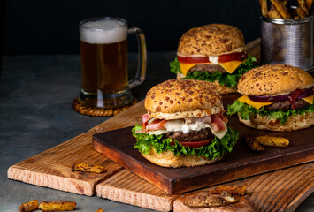 Closeup of delicious beef burgers served on two wooden boards with beer and fries in the background