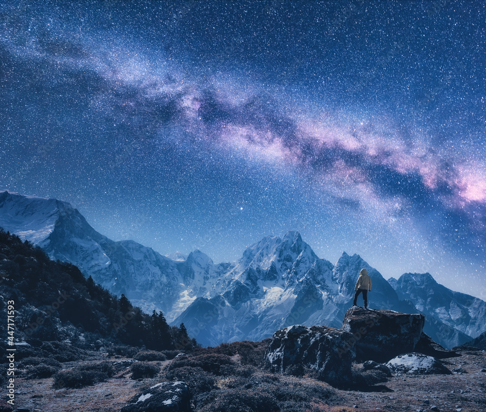 Silhouette of a standing man on the stone, mountains and starry sky with Milky Way at night in Nepal. Sky with stars. Travel. Night landscape with snow-covered rocks and purple milky way. Space - obrazy, fototapety, plakaty 
