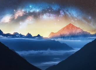 Wall Mural - milky way arch and snowy mountains in low clouds at starry night. landscape. sky with stars, arched 