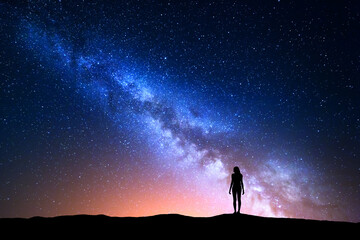 Wall Mural - Beautiful Milky Way with standing woman. Colorful landscape with night sky with stars and silhouette of a girl on hill on the background of beautiful galaxy. Blue milky way with yellow light. Space