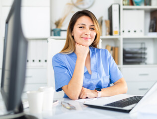 Wall Mural - Woman doctor in uniform is working behind laptop in clinic