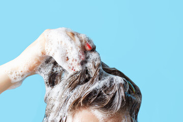 Girl washes her hair with shampoo on blue background, front view