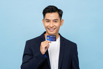 Wall Mural - Young handsome smiling Asian man in semi formal blazer holding credit card in light blue isolated studio background