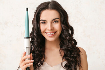 Wall Mural - Beautiful young woman with curling iron on light background