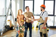 © Roman - Confident pleasant handyman holds out his hand for handshake with clients family, professional repairman in hardhat and overall at work, in new house. side view portrait