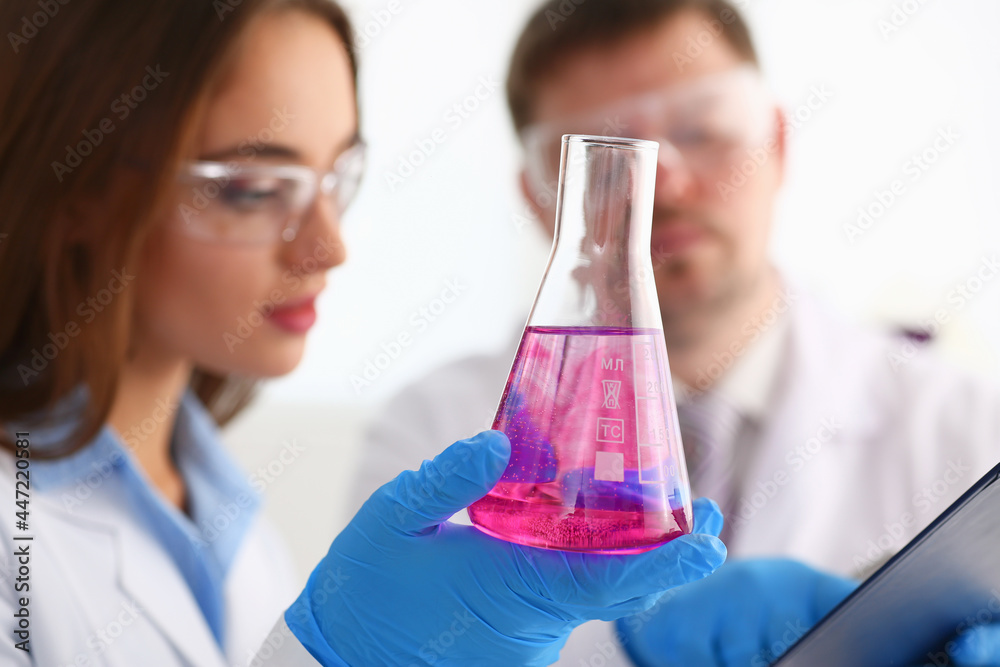 Female chemist holds test tube of glass in his hand overflows a liquid - obrazy, fototapety, plakaty 
