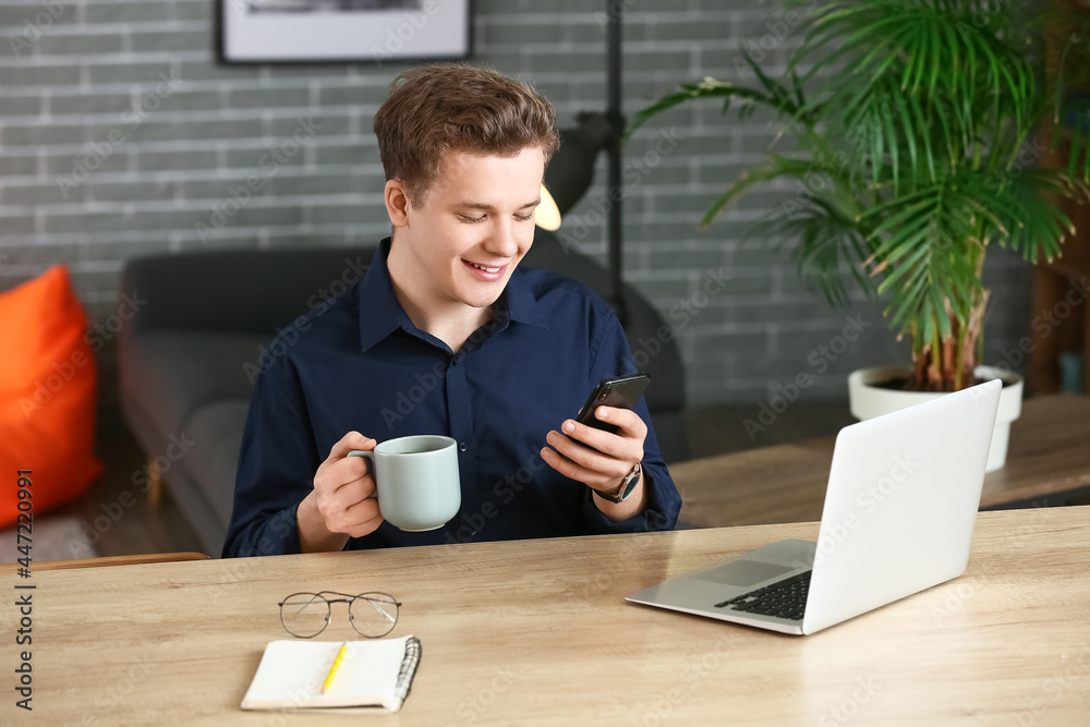 Young man drinking coffee while using mobile phone at home