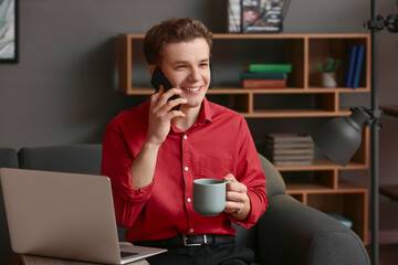 Wall Mural - Young man drinking coffee while talking by mobile phone at home