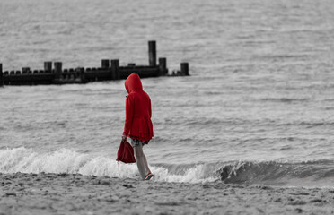 Wall Mural - back shot of man with red hoodie walking by the grayscale beach on a day, concept of loneliness