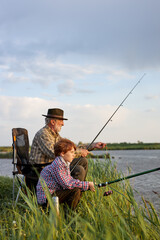 pleasant grandfather and grandson throwing fishing tackle in natural environment, on lake in nature,