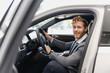© ViDi Studio - Side view smiling man customer buyer client in classic grey suit driving car hold wheel choose auto want buy new automobile in showroom vehicle salon dealership store motor show indoor Sale concept.