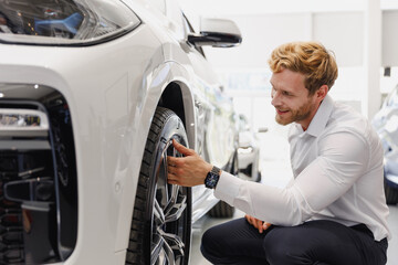 Wall Mural - Man happy smiling customer male buyer client wear white shirt touch tire wheel disc choose auto want buy new car automobile in showroom salon vehicle dealership store motor show indoor Sales concept