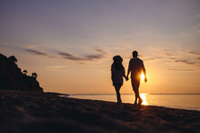 Full Body Back View Silhouette Young Couple Two Friends Family Man Woman In Casual Clothes Hold Hands Walk Stroll Together At Sunrise Over Sea Beach Ocean Outdoor Exotic Seaside In Summer Day Evening.