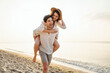 © ViDi Studio - Young excited couple two friends family man woman in casual clothes boyfriend give piggyback ride to joyful girlfriend sit on back at sunrise over sea beach ocean outside seaside in summer day evening
