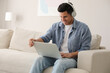 © New Africa - Man with laptop and headphones sitting on sofa at home