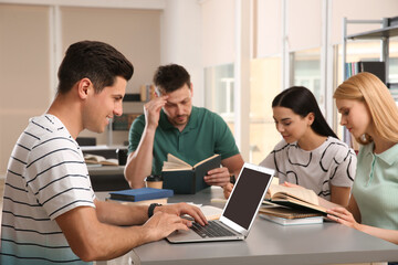 Poster - Young people discussing group project at table in library