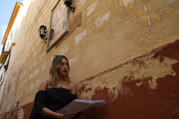 Portrait of a beautiful young woman. The woman is on holiday and is holding a map of the city she is visiting. The woman is on a street and above it you can see a mosaic with lanterns.