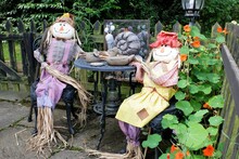 Two Scarecrow Figures Seated At Garden Table