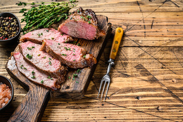 Wall Mural - Rare slices of Roast beef sirloin tri tip steak bbq on a wooden cutting board. wooden background. Top view. Copy space