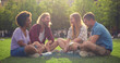 © TommyStockProject - Diverse young friends resting on green grass in park and talking