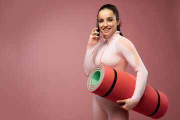 Wall Mural - Joyful young woman with yoga mat talking on cellphone