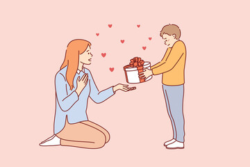 Wall Mural - Celebrating Happy Mothers day concept. Small smiling boy cartoon character standing giving present box to his young mother for holiday vector illustration 