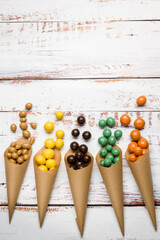 Wall Mural - Various flavors of chocolate pralines in paper cones on wooden table.