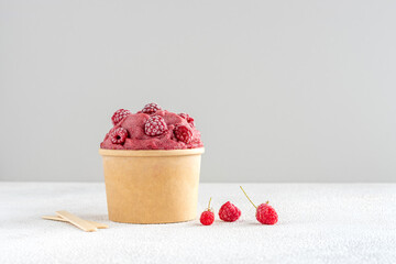 Red raspberry and banana vegan ice cream with frozen raspberries in paper bowl