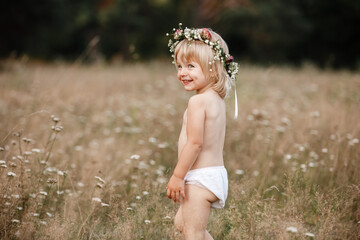 little beautiful girl on nature on summer day vacation. childgirl in panties and a flowers wreath on her head is playing in the field on summer day. The concept of family holiday and time together