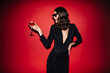 © Look! - Curly stylish elegant woman holds cocktail glass. Charming lady in sunglasses and black festive dress poses on red background.