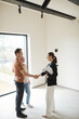 © Seventyfour - Vertical side view portrait of young couple shaking hands with real estate agent during apartment tour, copy space