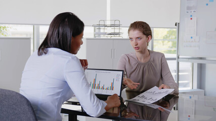 Wall Mural - African and caucasian female managers analyzing financial data on laptop and documents