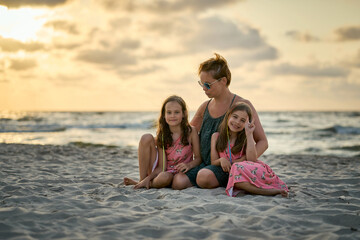 Wall Mural - Young happy beautiful mother and her daughters on the beach at sunset. 