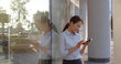 © TommyStockProject - Side view portrait young asian businesswoman using smartphone outside office building