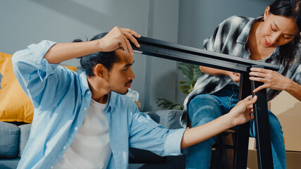 Wall Mural - Happy asian young attractive couple man and woman help each other unpacking box and assemble furniture decorate house build table with carton box in living room. Young married asian move home concept.