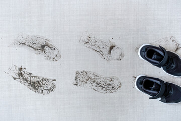 Dirty shoes leaving muddy footprints on carpet. top view